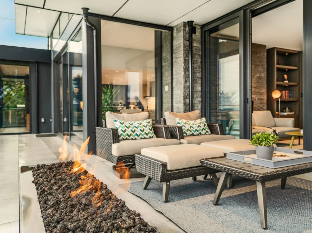 Outdoor space with fire pit and beige furniture looking into a home.